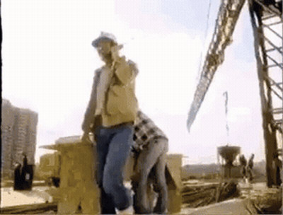 A Man In A Hard Hat Is Standing Next To A Woman In A Plaid Shirt On A Construction Site . GIF