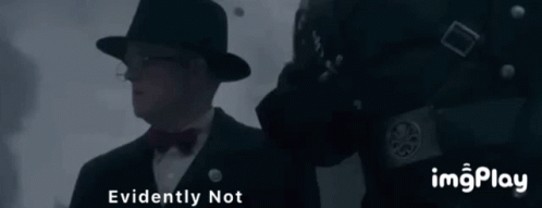 A Man In A Hat And Bow Tie Is Standing Next To A Man In A Black Uniform With The Words " Evidently Not " Above Him GIF