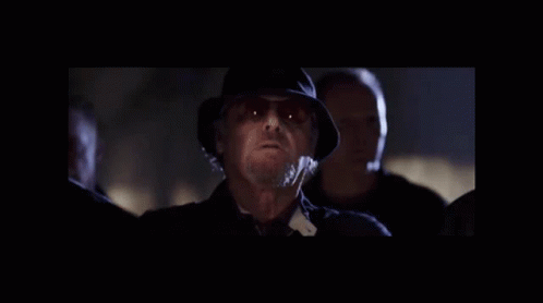 A Man In A Hat And Sunglasses Is Standing In A Dark Room . GIF