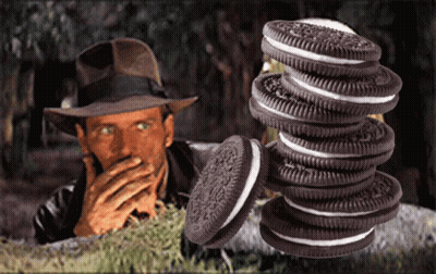 A Man In A Hat Is Covering His Mouth Behind A Stack Of Oreos GIF