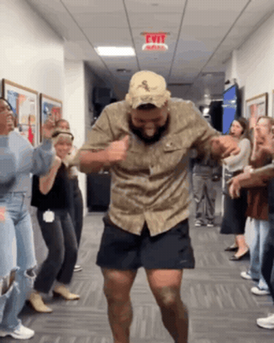 A Man In A Hat Is Dancing In A Hallway With A Group Of People . GIF