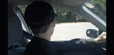 A Man In A Hat Is Driving A Car And Looking Out The Window GIF