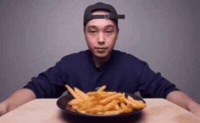 A Man In A Hat Is Eating French Fries From A Plate . GIF