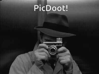 A Man In A Hat Is Holding A Camera In Front Of His Face With The Words Picdoot Below Him GIF