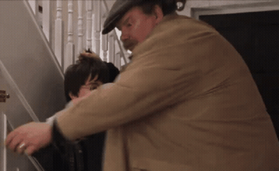A Man In A Hat Is Holding A Child 'S Head While Standing On A Set Of Stairs . GIF