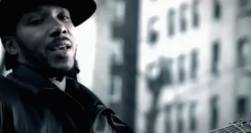 A Man In A Hat Is Holding A Guitar In Front Of A Building That Says 616 GIF
