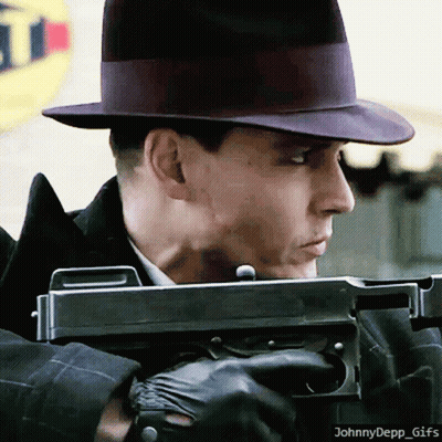 A Man In A Hat Is Holding A Gun In Front Of A Sign That Says ' T ' On It GIF