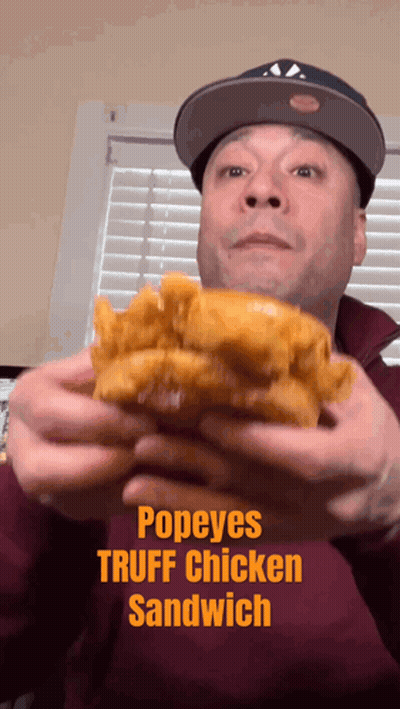 A Man In A Hat Is Holding A Popeye 'S Truffle Chicken Sandwich GIF