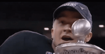 A Man In A Hat Is Holding A Trophy With A Football In His Hand . GIF
