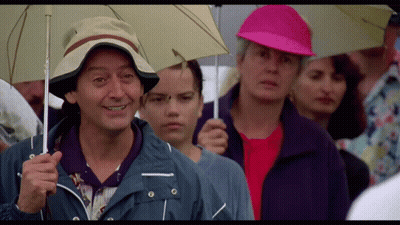 A Man In A Hat Is Holding An Umbrella In A Crowd GIF