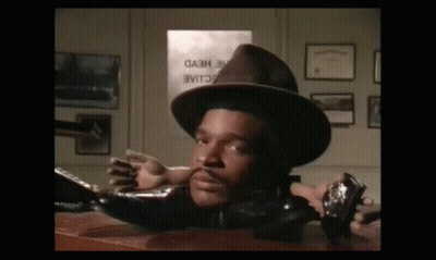 A Man In A Hat Is Laying On A Desk In Front Of A Sign That Says " Cash " GIF