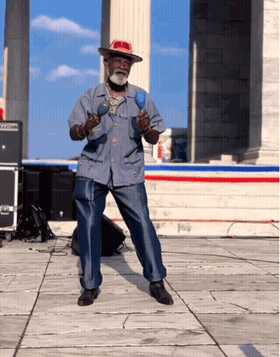 A Man In A Hat Is Playing Maracas On A Stage GIF