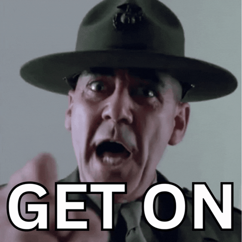 A Man In A Hat Is Pointing With The Word Get On Below Him GIF