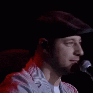 A Man In A Hat Is Singing Into A Microphone . GIF