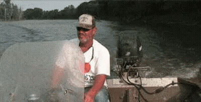 A Man In A Hat Is Sitting In A Boat On A Lake GIF