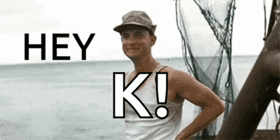 A Man In A Hat Is Standing In Front Of A Body Of Water And Says Hey K! GIF
