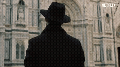A Man In A Hat Is Standing In Front Of A Building That Says Netflix On The Bottom GIF