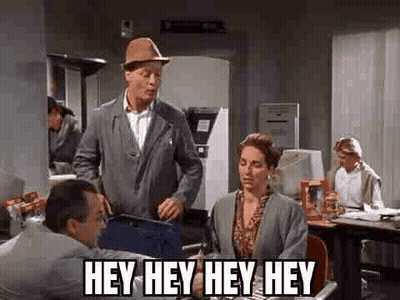 A Man In A Hat Is Standing Next To A Woman In An Office And Talking To Her . GIF