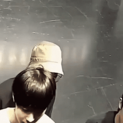 A Man In A Hat Is Standing Next To Another Man In A Room . GIF