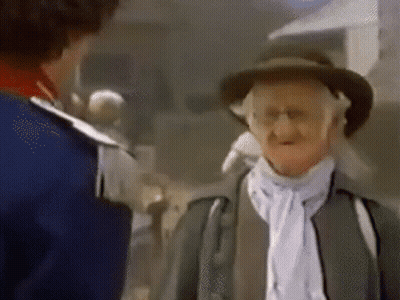 A Man In A Hat Is Talking To Another Man In A Blue Jacket . GIF