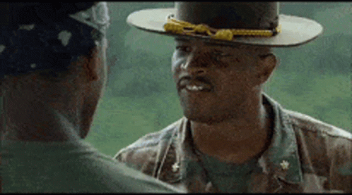 A Man In A Hat Is Talking To Another Man In A Camouflage Uniform GIF