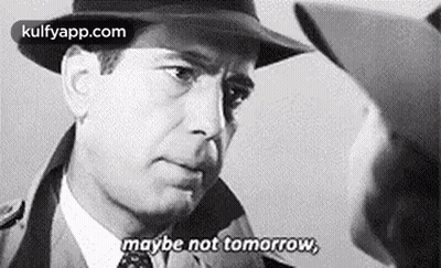 A Man In A Hat Is Talking To Another Man In A Suit And Tie . GIF