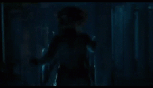 A Man In A Hat Is Walking Through A Doorway In A Room . GIF
