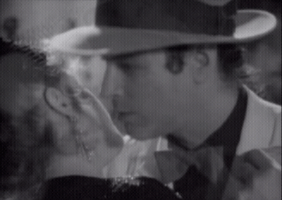 A Man In A Hat Kisses A Woman In A Black And White Photo GIF