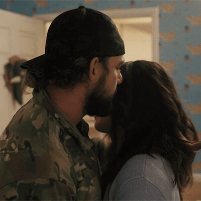 A Man In A Hat Kisses A Woman In A Blue Shirt GIF
