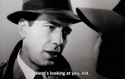 A Man In A Hat Says " Here 'S Looking At You Kid " To Another Man GIF