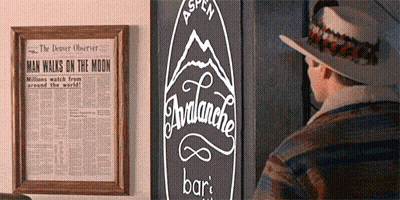 A Man In A Hat Stands In Front Of A Newspaper That Says Man Walks On The Moon GIF