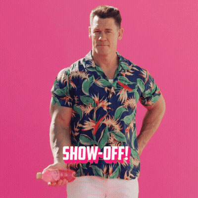 A Man In A Hawaiian Shirt Holds A Pink Object In Front Of A Pink Background That Says Show-Off GIF
