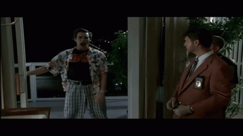 A Man In A Hawaiian Shirt Is Holding A Knife While Standing Next To A Man In A Suit And Tie . GIF