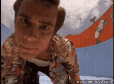 A Man In A Hawaiian Shirt Is Looking Down At The Camera With A Banner In The Background That Says Mortmernova.com GIF