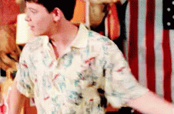 A Man In A Hawaiian Shirt Is Standing In Front Of An American Flag GIF