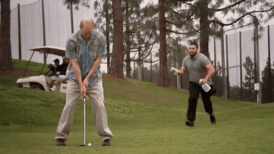 A Man In A Hawaiian Shirt Is Swinging A Golf Club On A Golf Course GIF