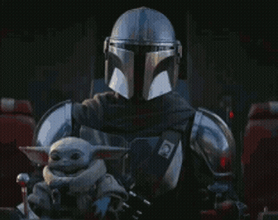 A Man In A Helmet Is Holding A Baby Yoda In His Lap . GIF