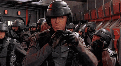A Man In A Helmet Is Holding A Gun In Front Of A Group Of Soldiers GIF