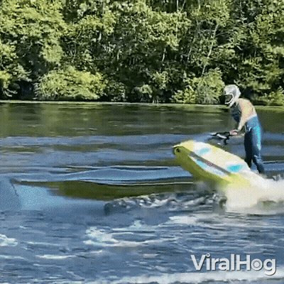 A Man In A Helmet Is Riding A Jet Ski In A Lake . GIF