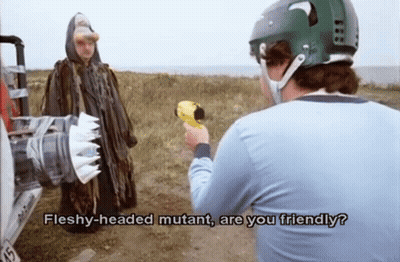 A Man In A Helmet Is Talking To A Fleshy-Headed Mutant Holding A Gun GIF