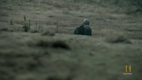 A Man In A Helmet Is Walking In A Field With A History Logo In The Corner GIF