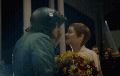 a man in a helmet kisses a woman holding flowers