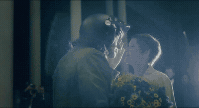 A Man In A Helmet Kisses A Woman With Flowers GIF