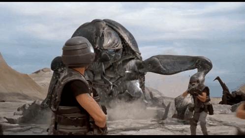 A Man In A Helmet Stands In Front Of A Giant Robot GIF