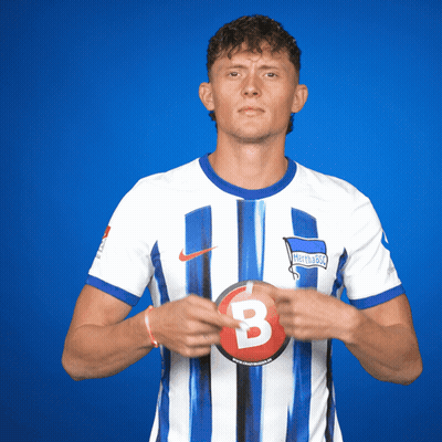 A Man In A Hertha Berlin Jersey Holds A Red B GIF