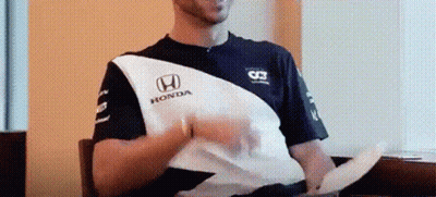 A Man In A Honda Shirt Is Sitting On A Couch Holding A Piece Of Paper . GIF