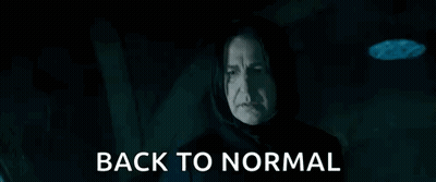A Man In A Hood Is Holding A Glass And Says `` Back To Normal '' In A Dark Room . GIF