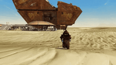 A Man In A Hood Is Walking In The Sand Near A Large Building GIF