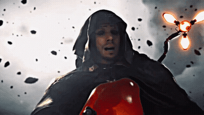 A Man In A Hooded Cape Holds A Red Object In His Hand GIF