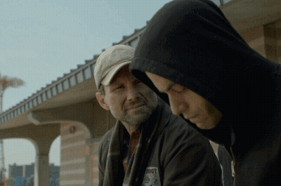A Man In A Hooded Jacket Has A Patch On His Jacket That Says ' Roots ' On It GIF